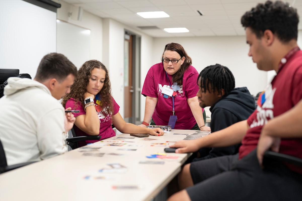 Students and a professor look at cards on a table intently